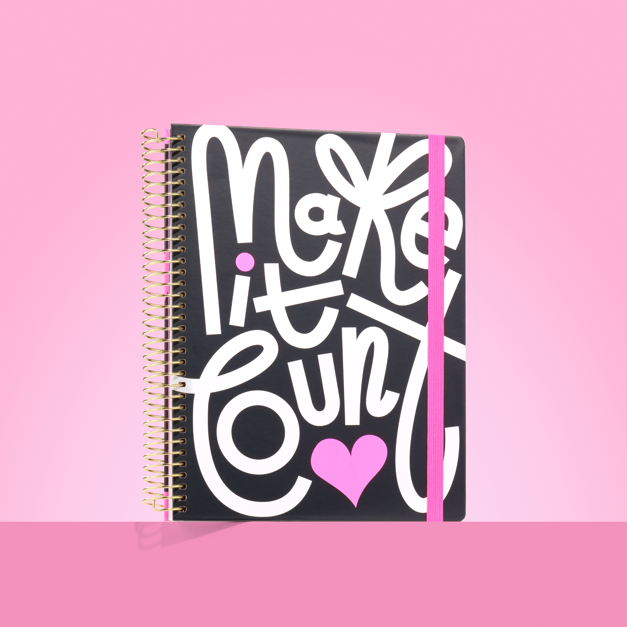 Black 2026 spiral-bound planner with bold white "Make it Count" lettering, pink heart, and pink elastic closure on a pink background.