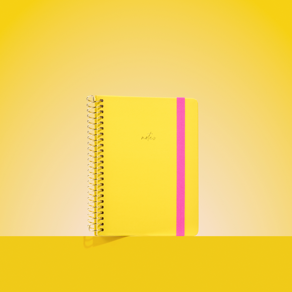 Bright yellow 2026 notepad with gold spiral binding, hot pink elastic closure, and "notes" embossed in gold on the cover.