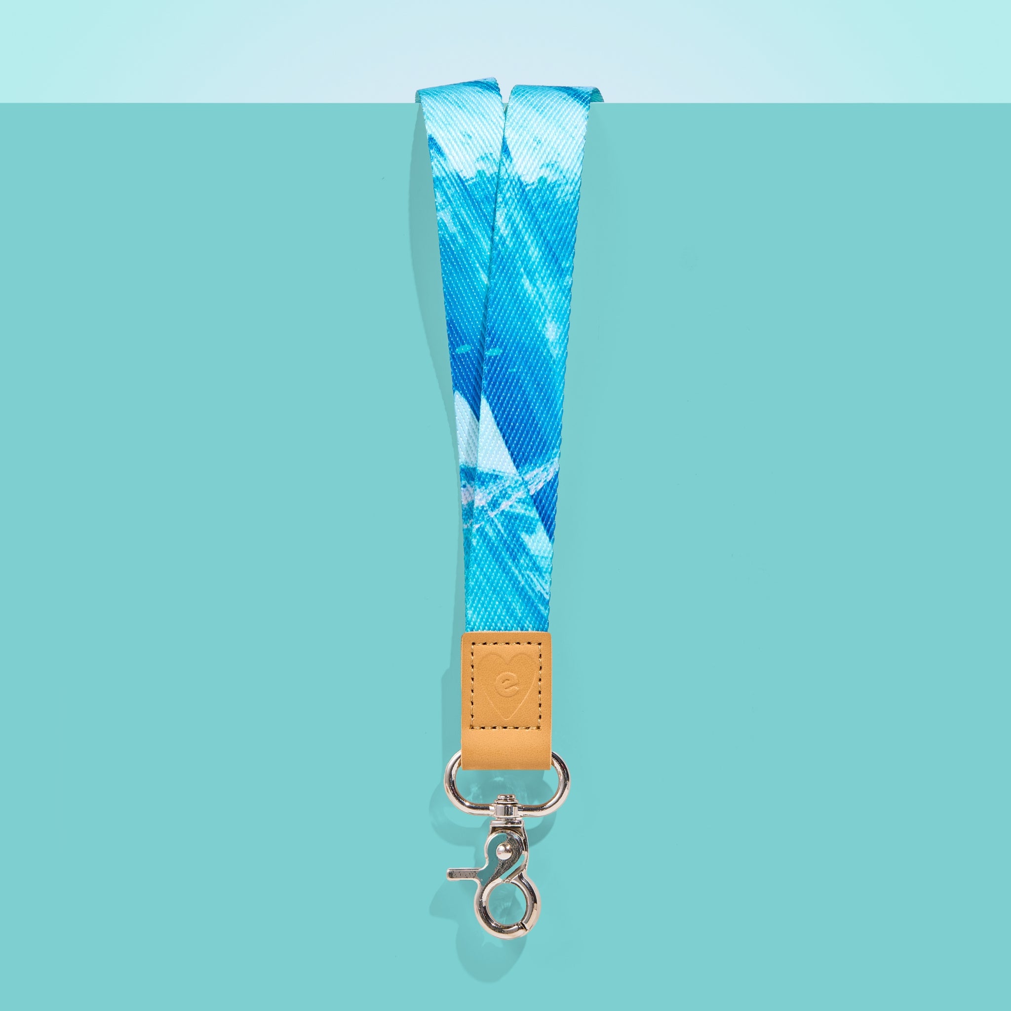 Blue and white patterned teacher lanyard with tan leather accent and silver clasp, displayed on a teal background.