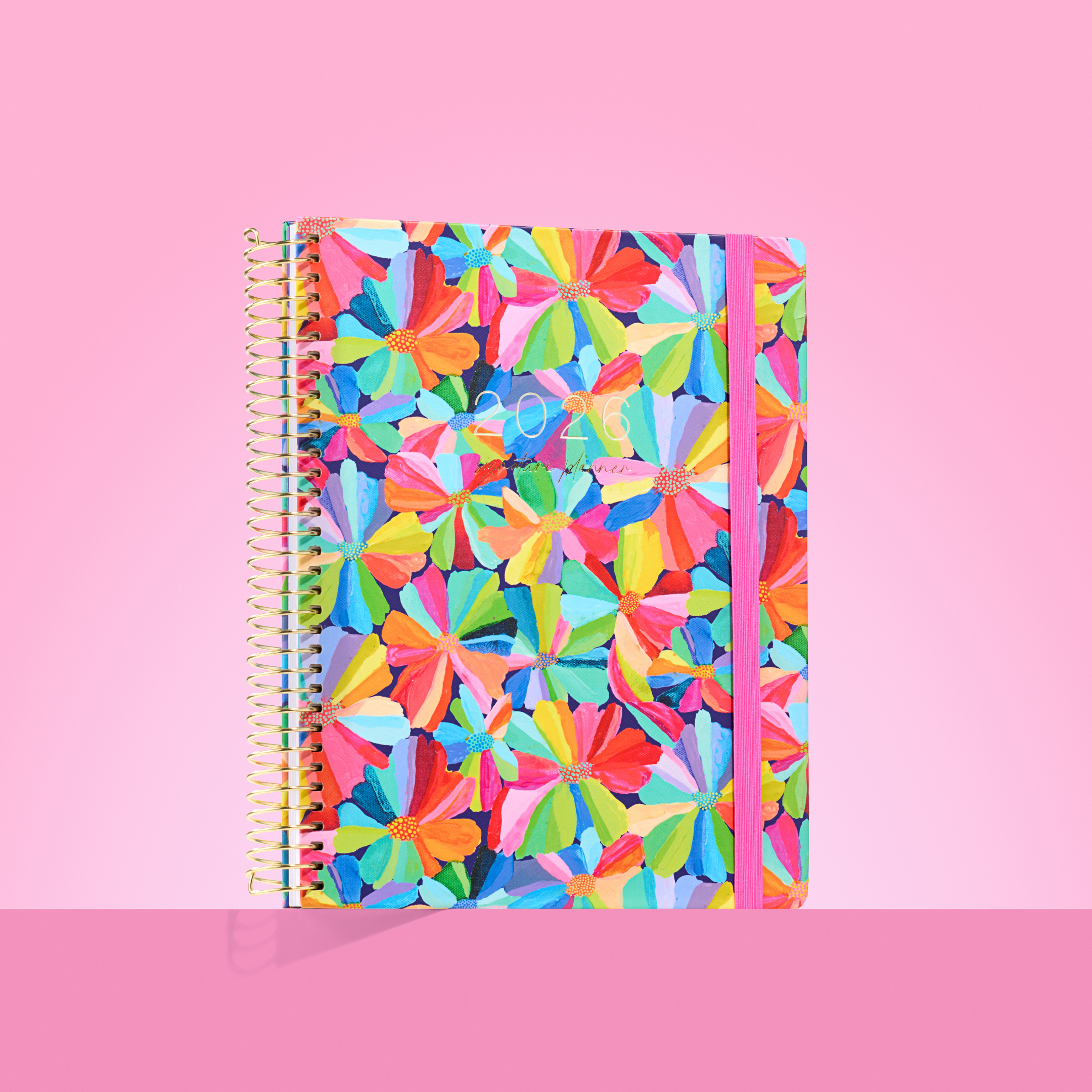 2026 teacher planner with bold multicolour petal design, gold spiral binding, and hot pink elastic strap.