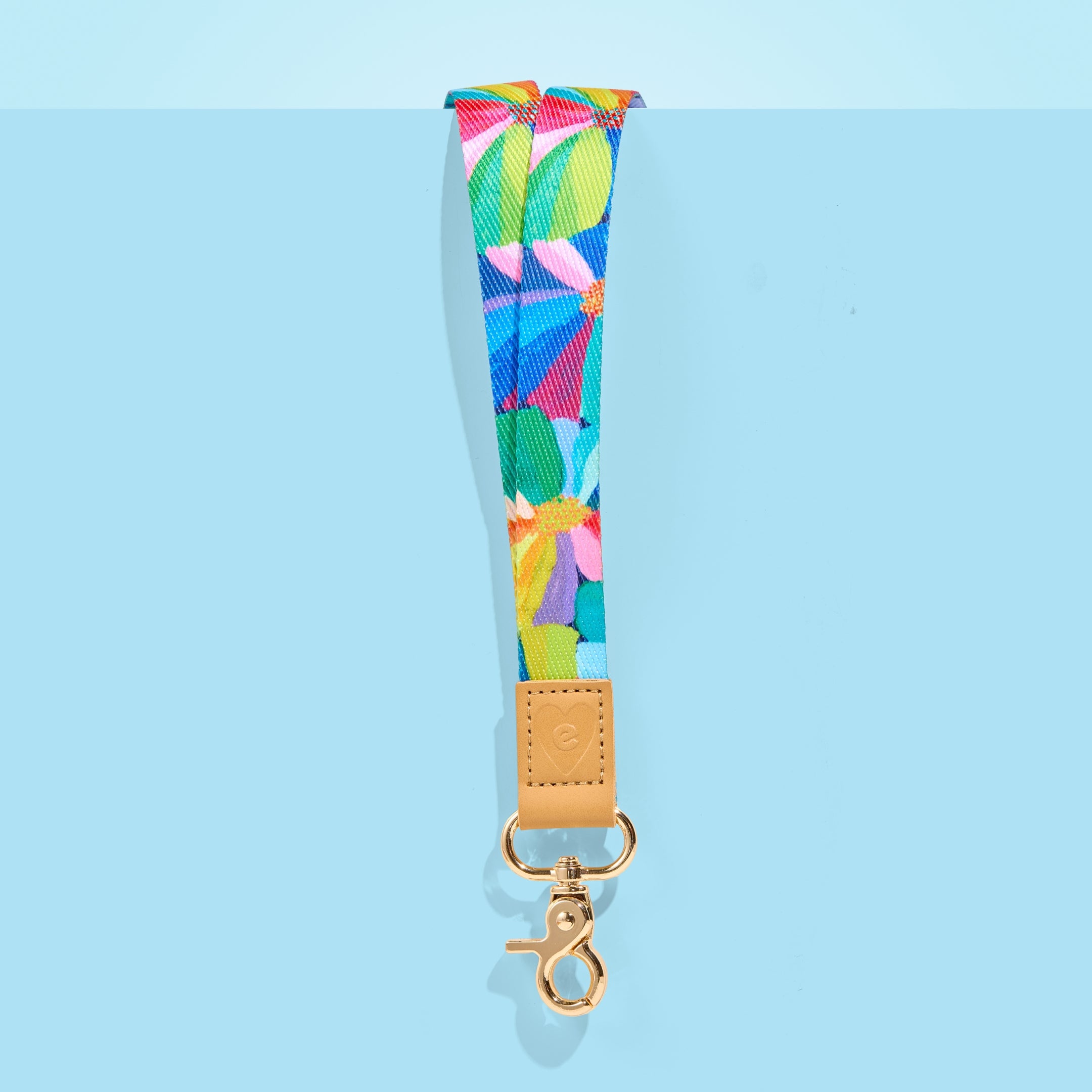 Bright floral teacher lanyard with tan leather accent and gold clasp, displayed on a light blue background.