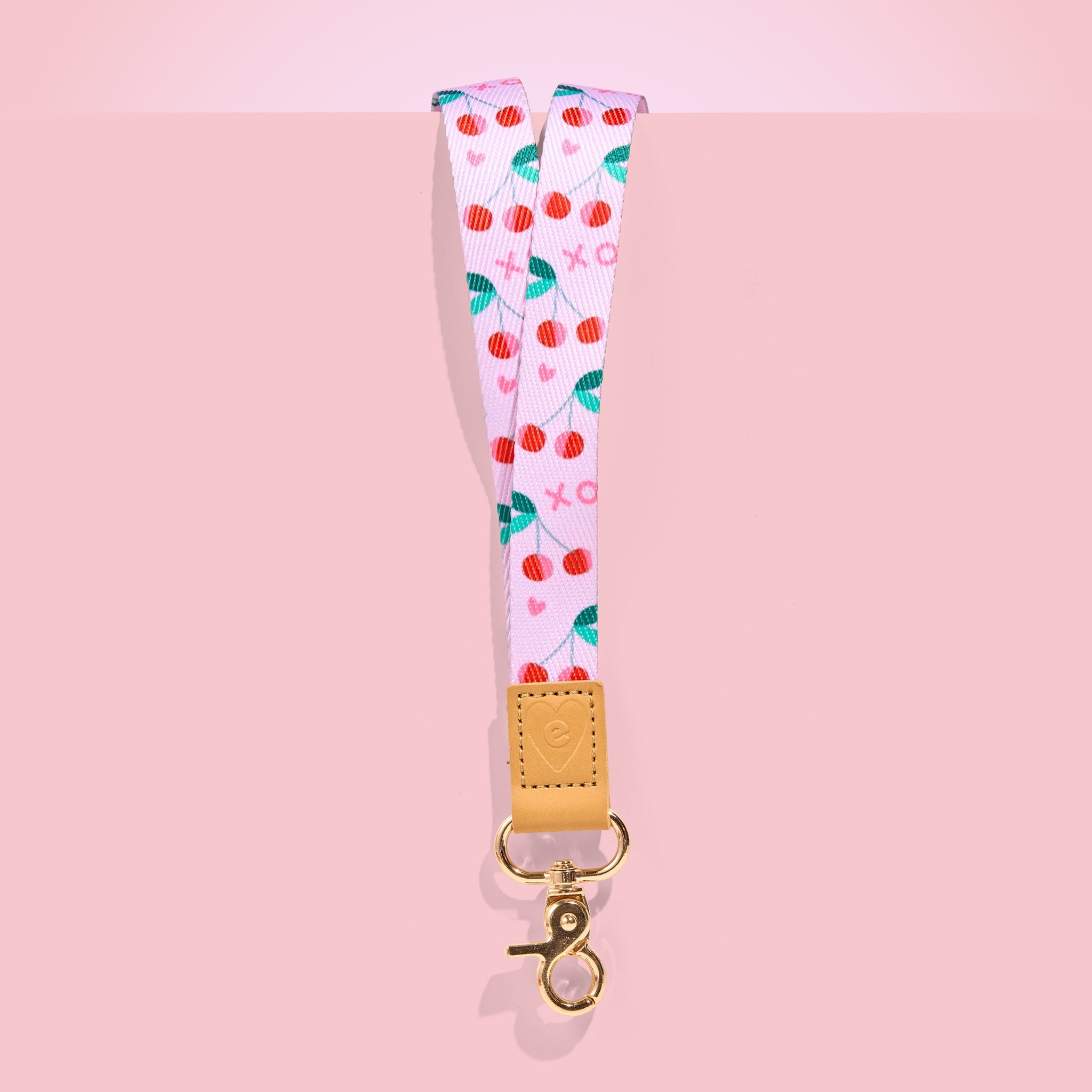 Pink teacher lanyard with red cherry pattern, tan leather accent and gold clasp, displayed on a blush pink background.