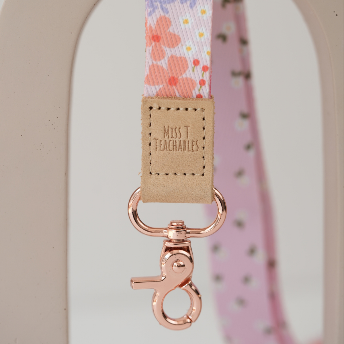 Close up of Pink Ditsy Floral lanyard clasp, embossed Miss T Teachables tan tab and rose gold swivel clasp
