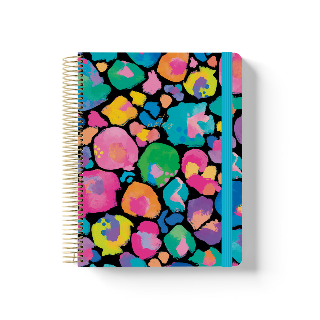 Black coiled notebook with rainbow leopard print, gold spiral binding, bright blue elastic band, and “notes” in gold script.
