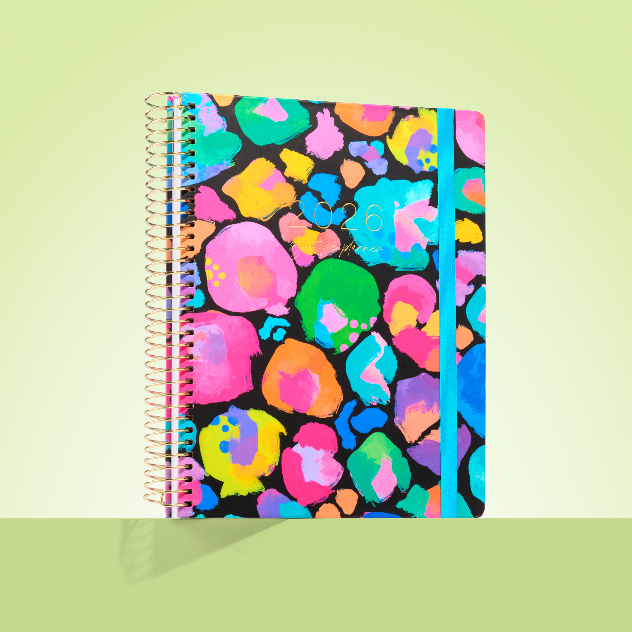 2026 teacher planner with vibrant rainbow leopard print, gold coil binding, and a bright blue elastic strap.