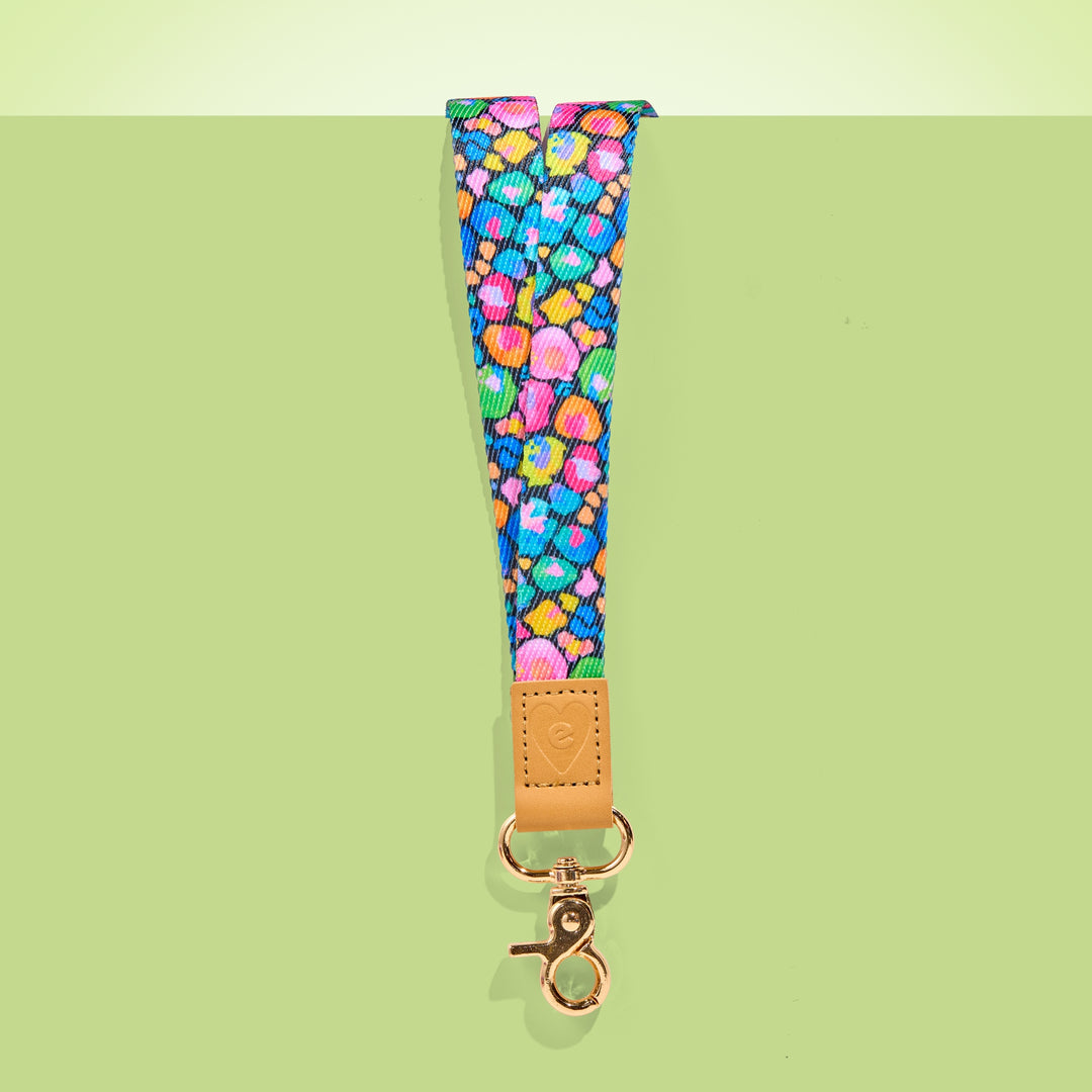 Colourful teacher lanyard with playful pattern, tan leather accent and gold clasp, shown on a light green background.