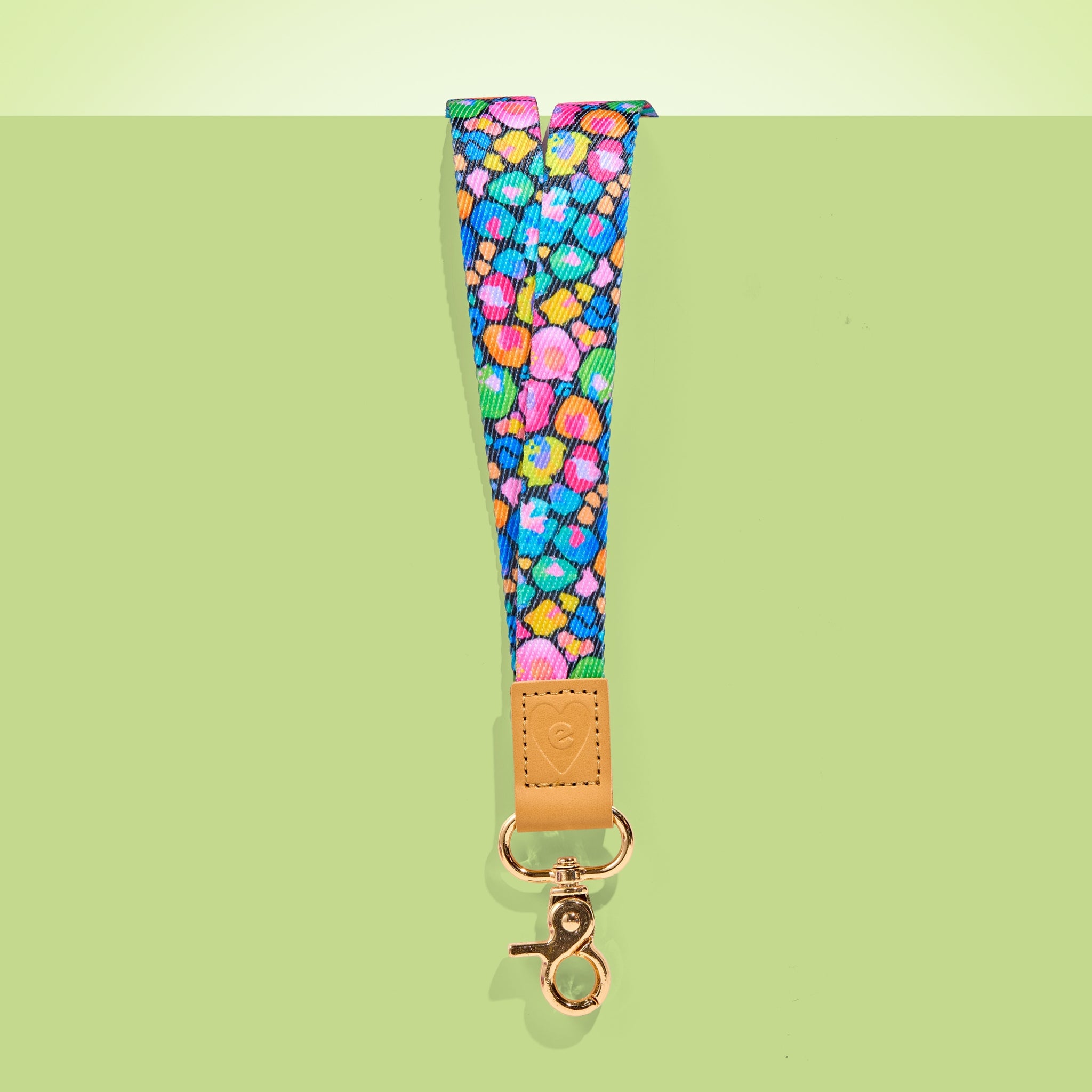 Colourful teacher lanyard with playful pattern, tan leather accent and gold clasp, shown on a light green background.
