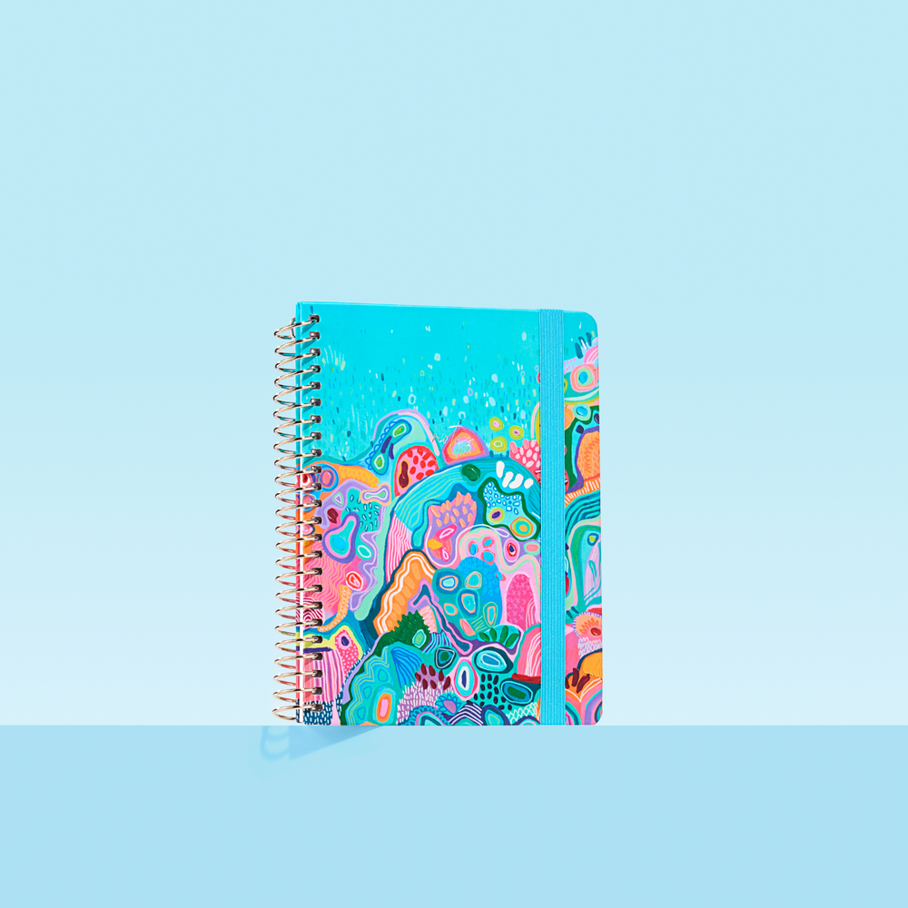 Bright blue 2026 notepad with reef-inspired abstract artwork, silver spiral binding, and matching blue elastic closure on light blue background.