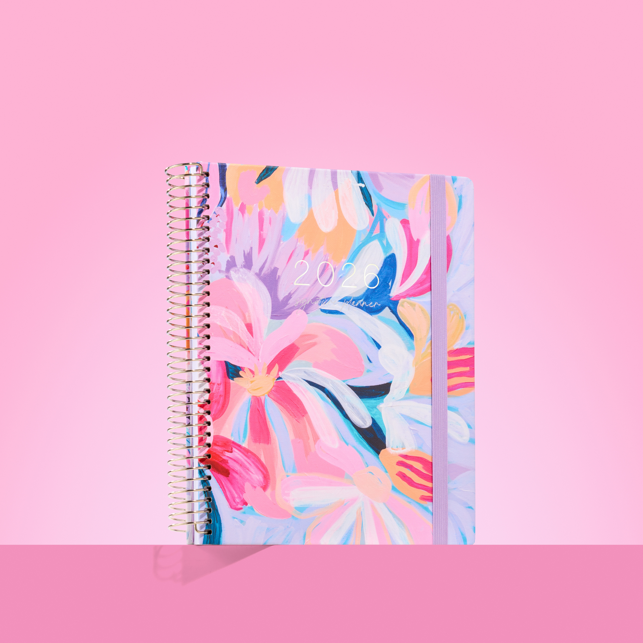  2026 teacher planner with large painted florals in pink, purple, blue and orange tones, pink elastic strap and silver coil.
