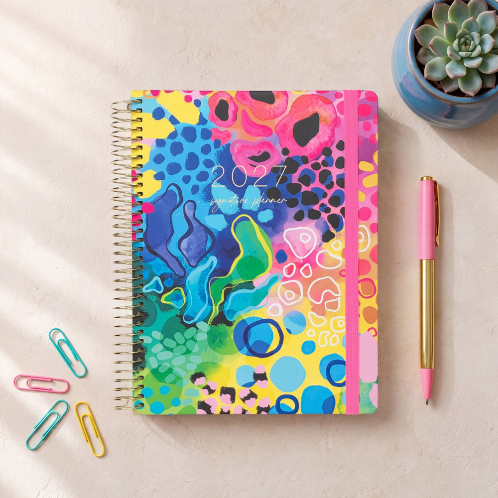 2027 Signature Planner in Boom styled with colourful paper clips and a pink pen, gold coil and pink elastic closure.