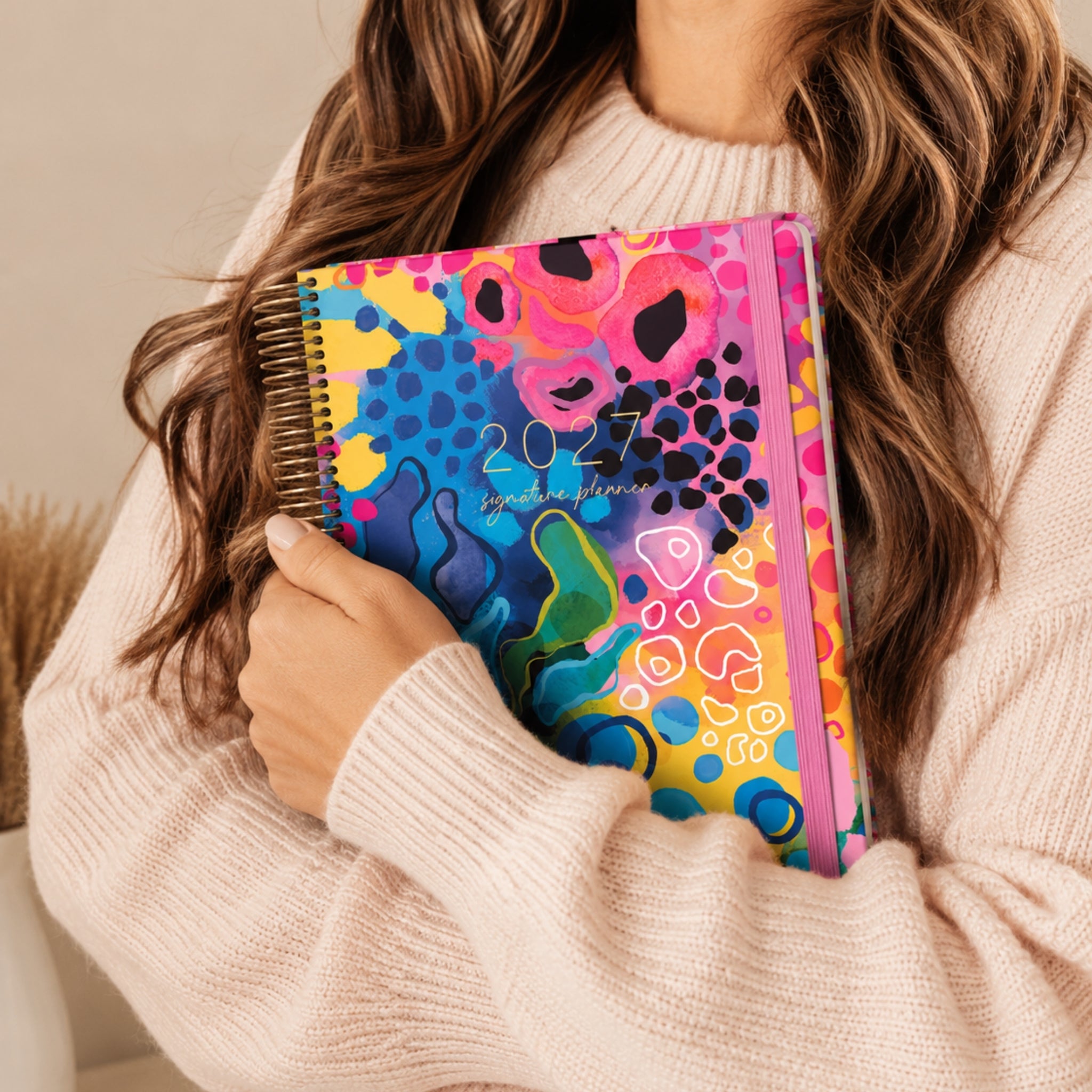 2027 Signature Planner in Boom held by a woman in a cream knit sweater, gold coil and pink elastic closure.