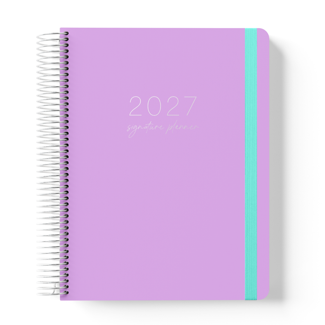 2027 Signature Daily Planner in Lilac with tonal text on a soft purple cover, silver coil binding, and teal elastic closure.