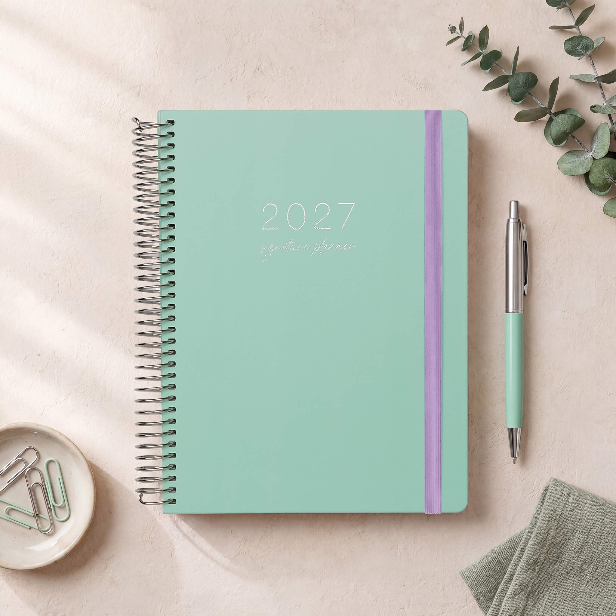 2027 Signature Planner in Seafoam styled with eucalyptus and a mint pen, silver coil and lilac elastic closure.