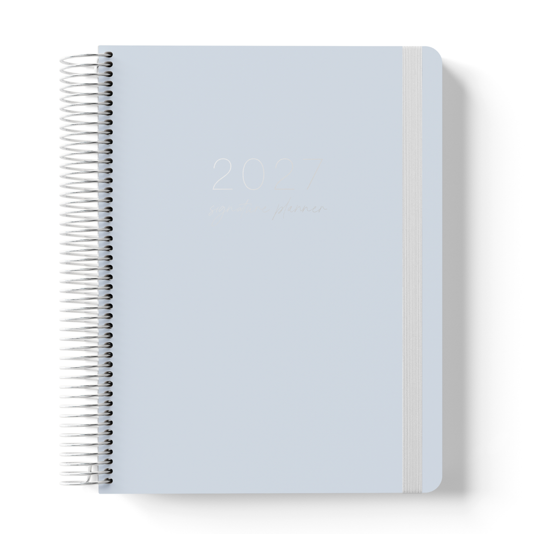 2027 Signature Planner in Dusk with tonal text on a soft blue-grey cover, silver coil binding, and matching grey elastic closure.