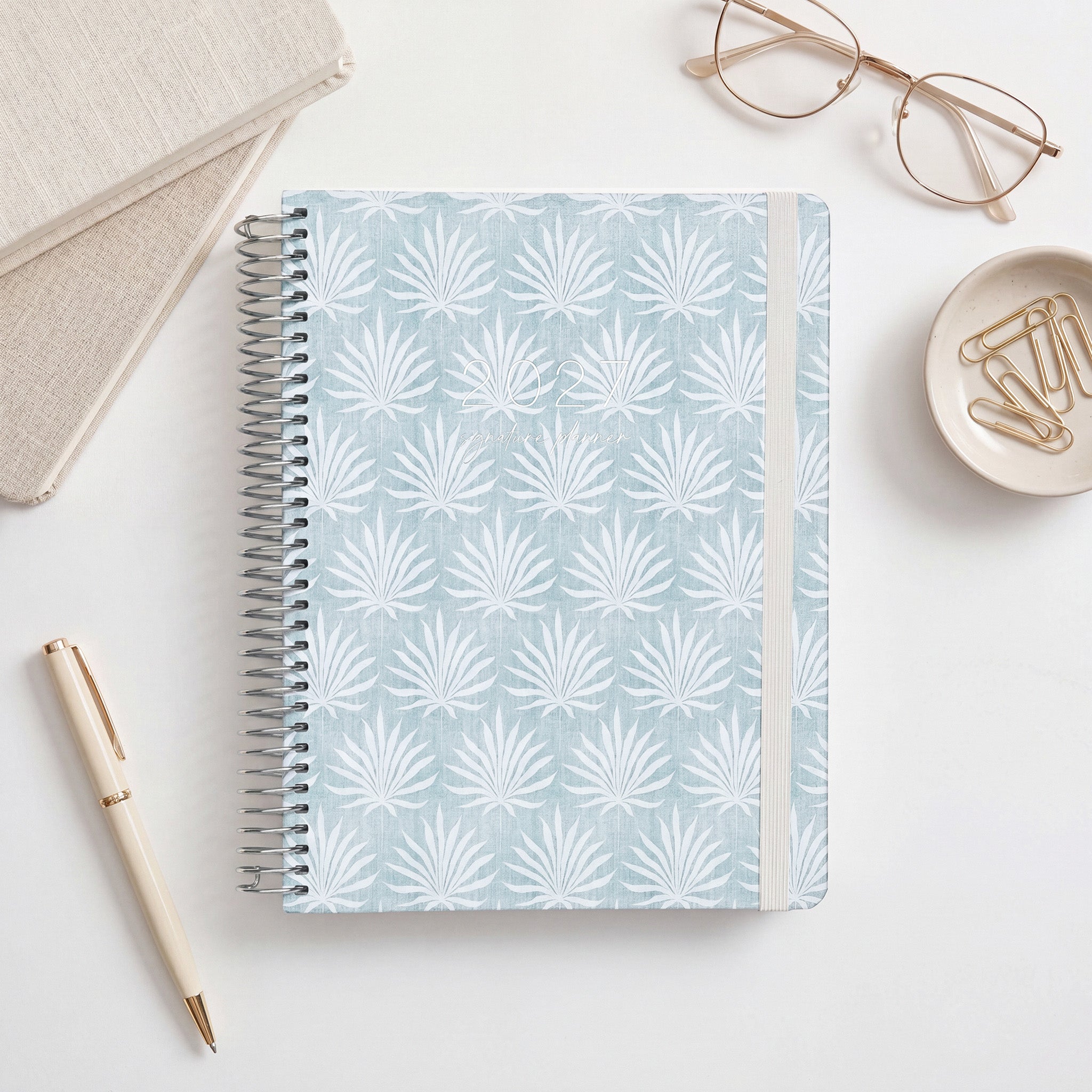 2027 Signature Planner in Palms with white palm frond pattern on blue-grey, silver coil and cream elastic closure.