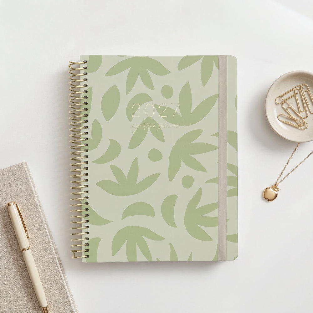2027 Signature Planner in Sunburst Sage with sage botanical leaf pattern on pale green, gold coil and cream elastic closure.