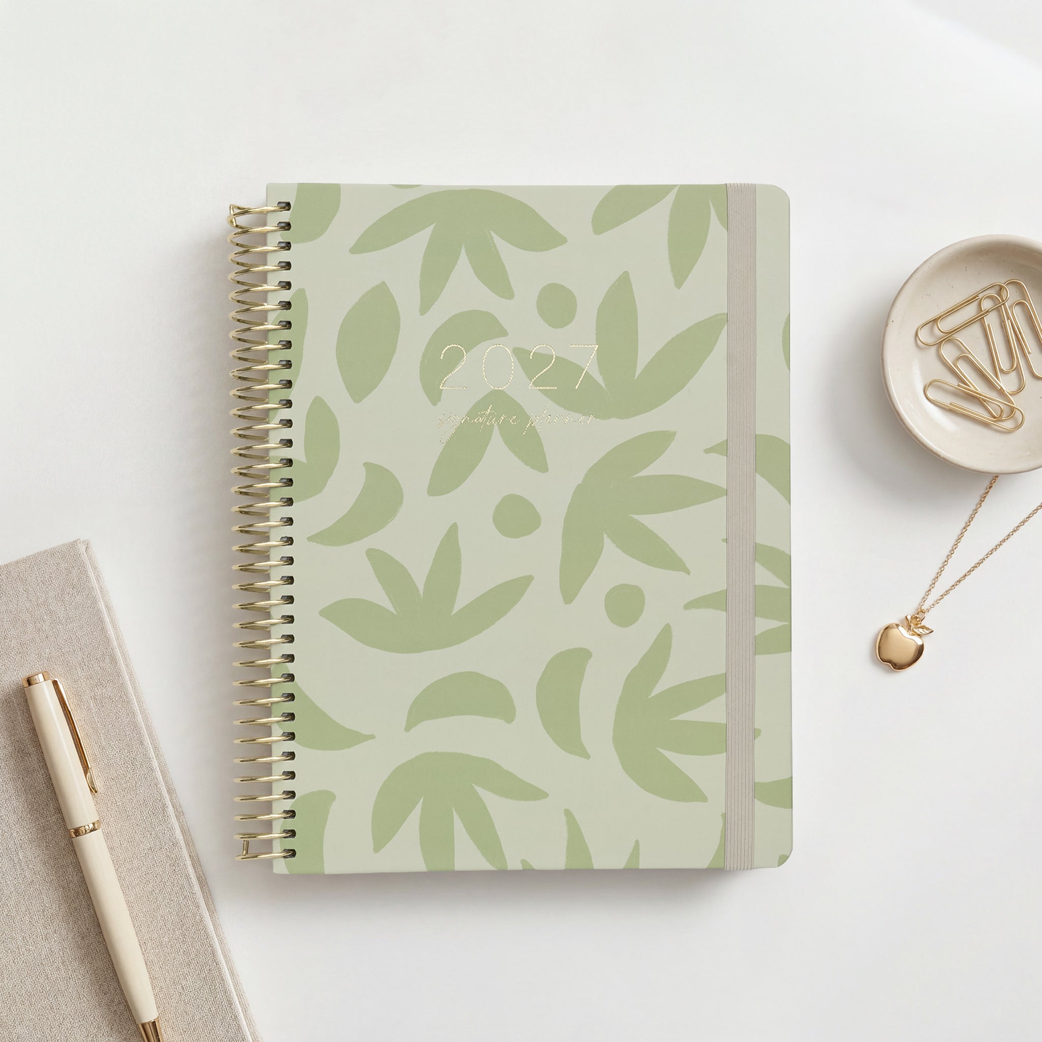 2027 Signature Planner in Sunburst Sage with sage botanical leaf pattern on pale green, gold coil and cream elastic closure.