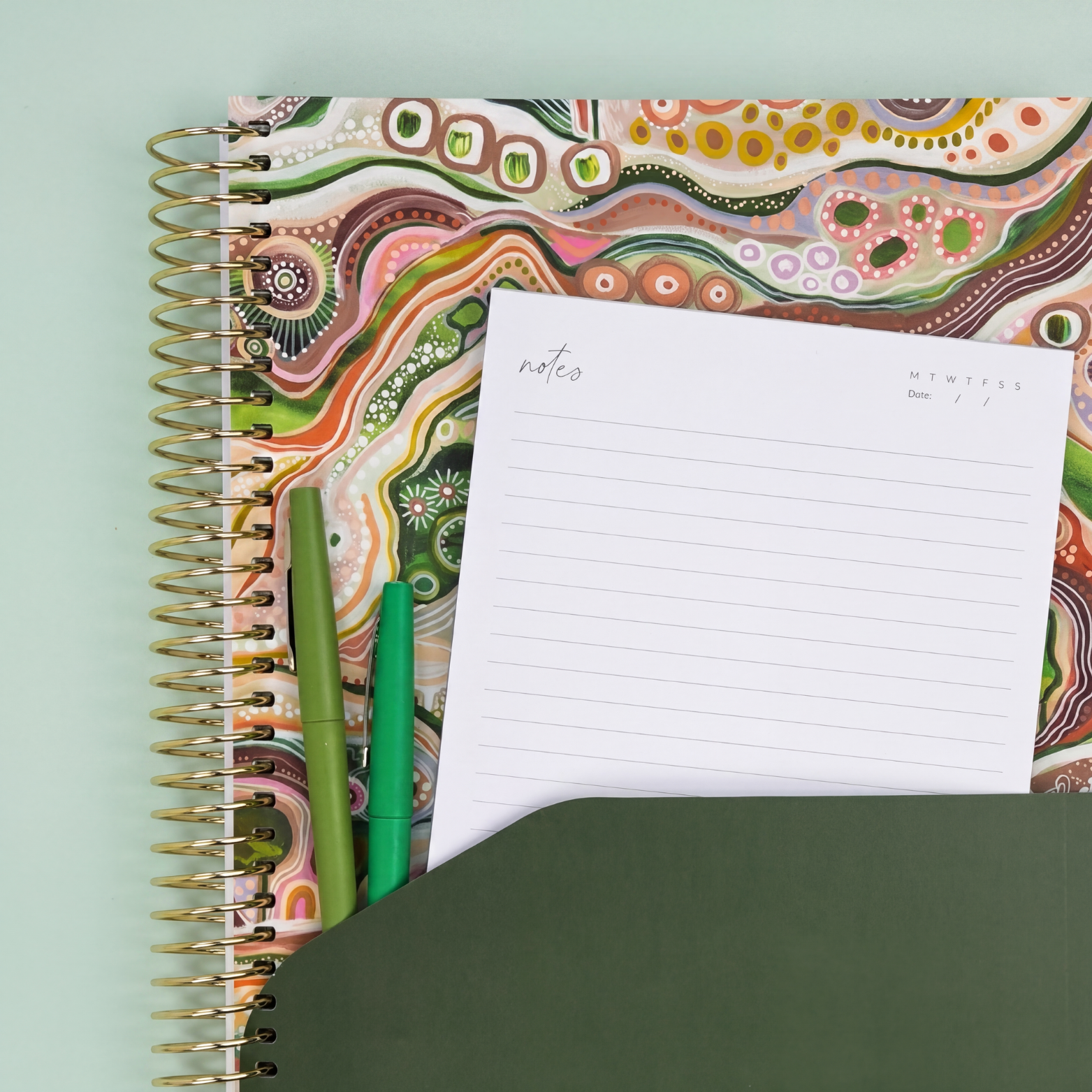 2027 Sacred Grandparent Tree Weekly Teacher Planner showing green pocket sleeve with notes, pens and gold coil on white background.