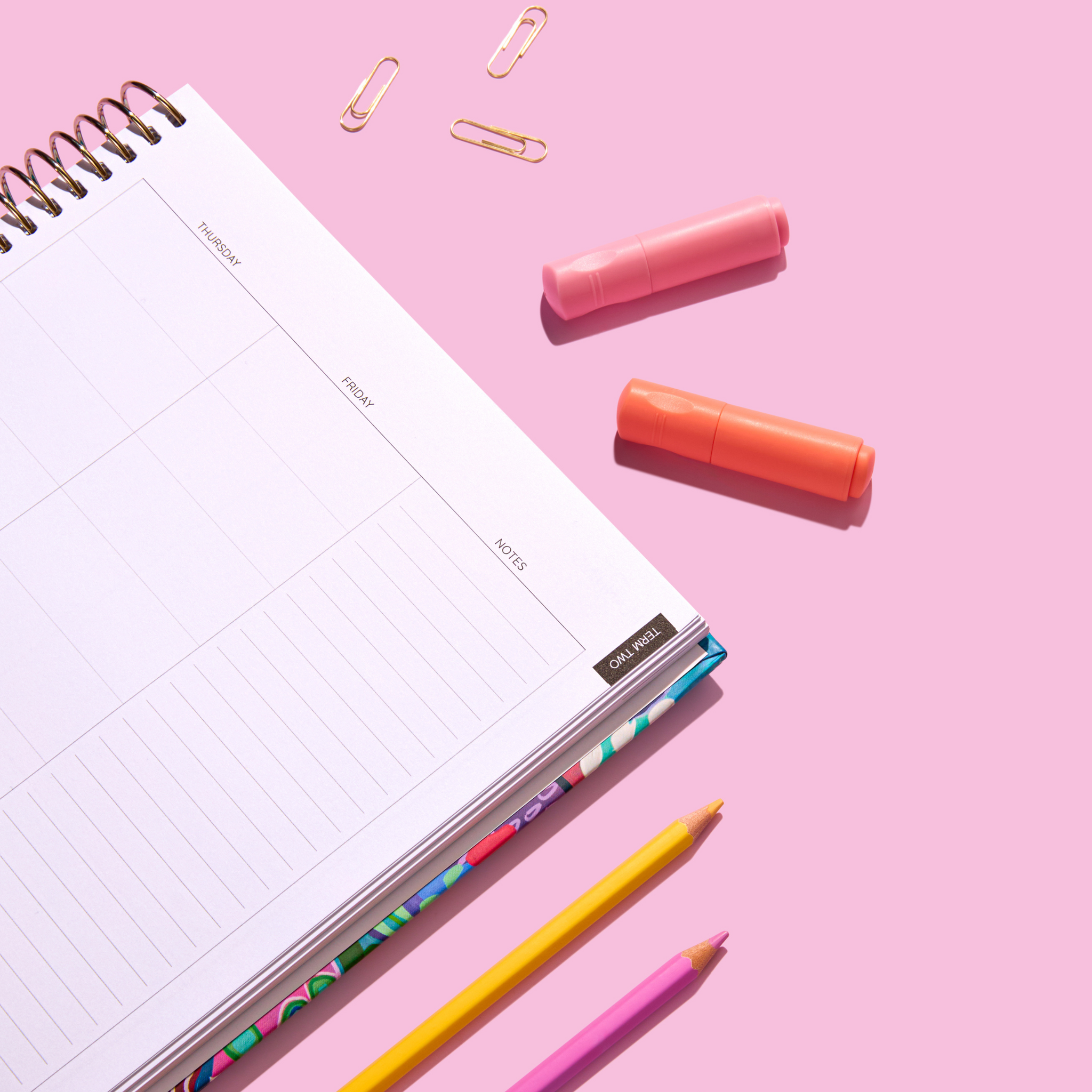 Close-up of a 2026 teacher planner open to a weekly spread, showing Thursday to Friday and a notes section, surrounded by highlighters, pencils, and paper clips on a pink background.