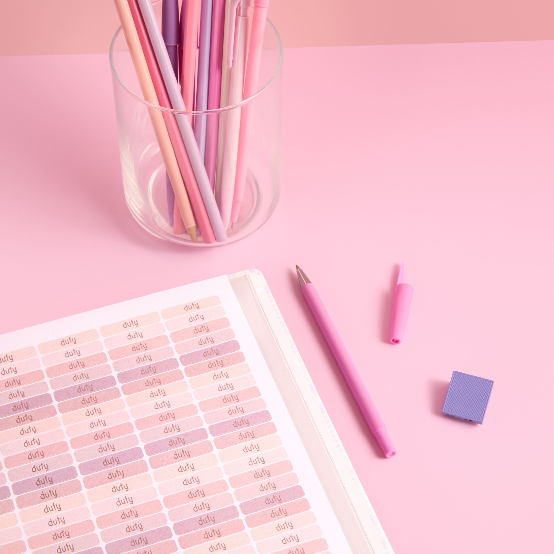 Pink “duty” planner stickers, pastel pens in a clear cup, and pink stationery on a soft pink background.