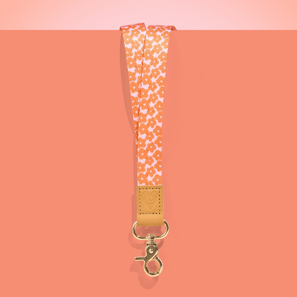 Orange and white patterned teacher lanyard with tan leather accent and gold clasp, displayed on a coral background