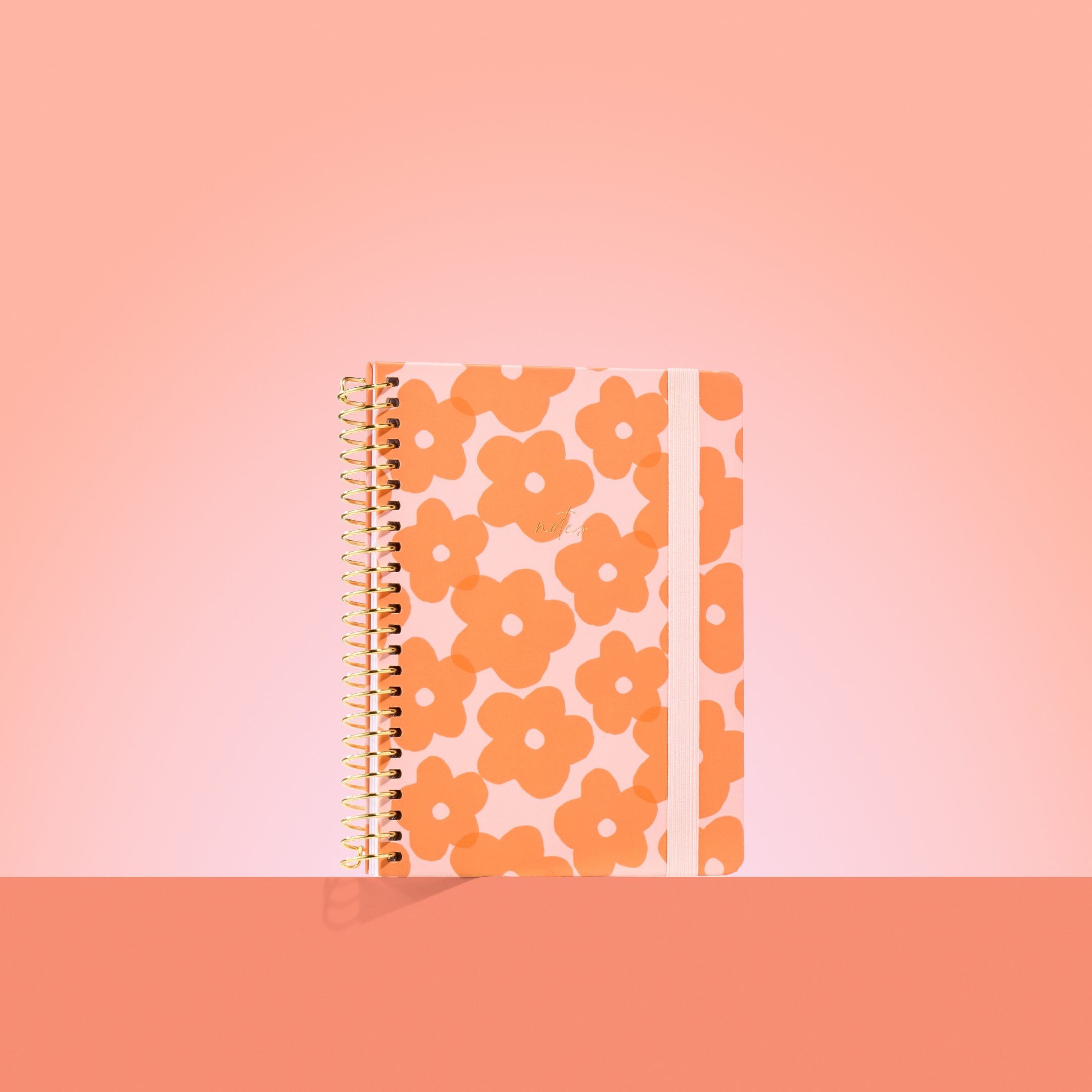 Peach-toned 2026 notepad with bold orange flower pattern, gold spiral binding, pale pink elastic closure, and gold "notes" text.