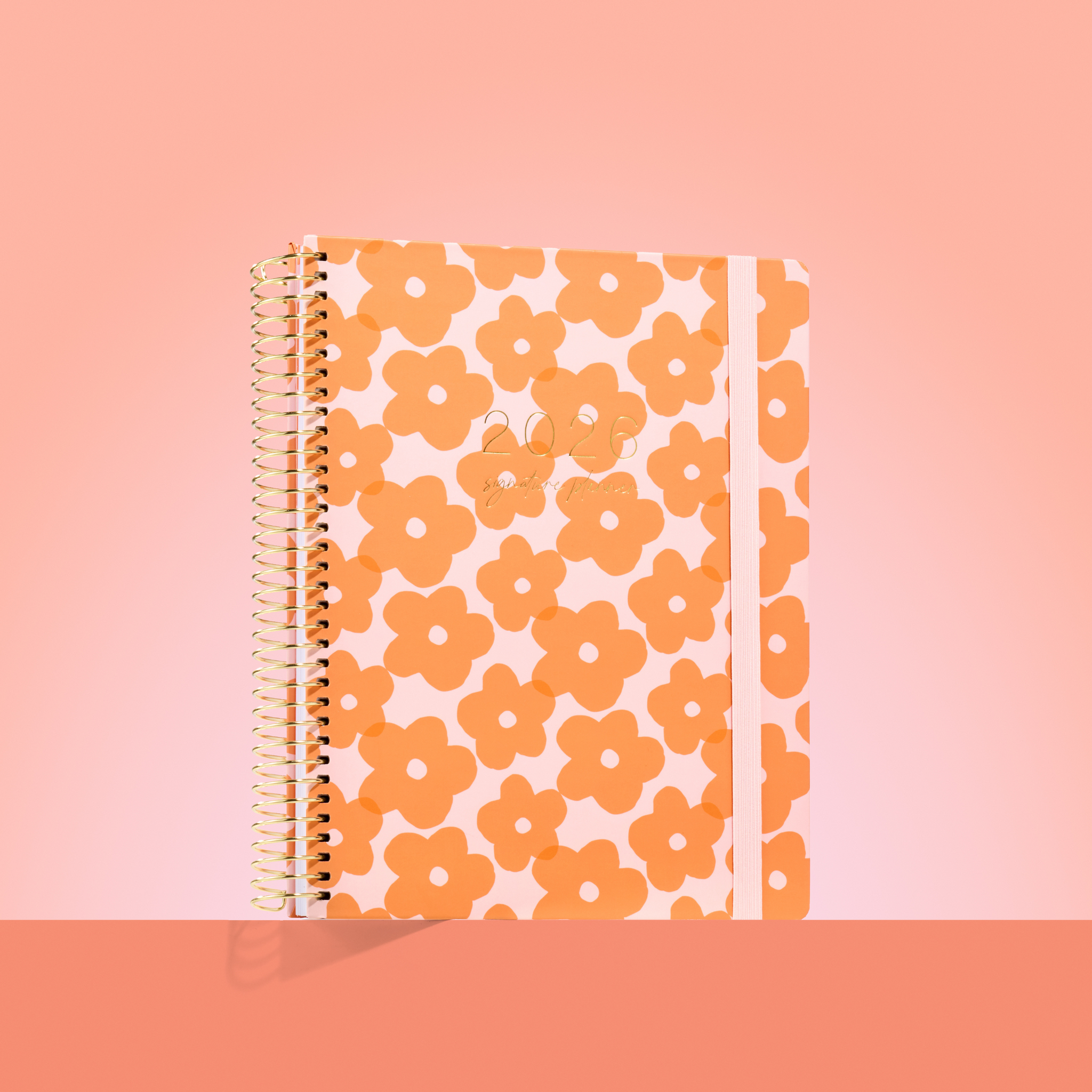 2026 teacher planner with bold tangerine flower pattern, gold coil binding, and pale peach elastic strap.
