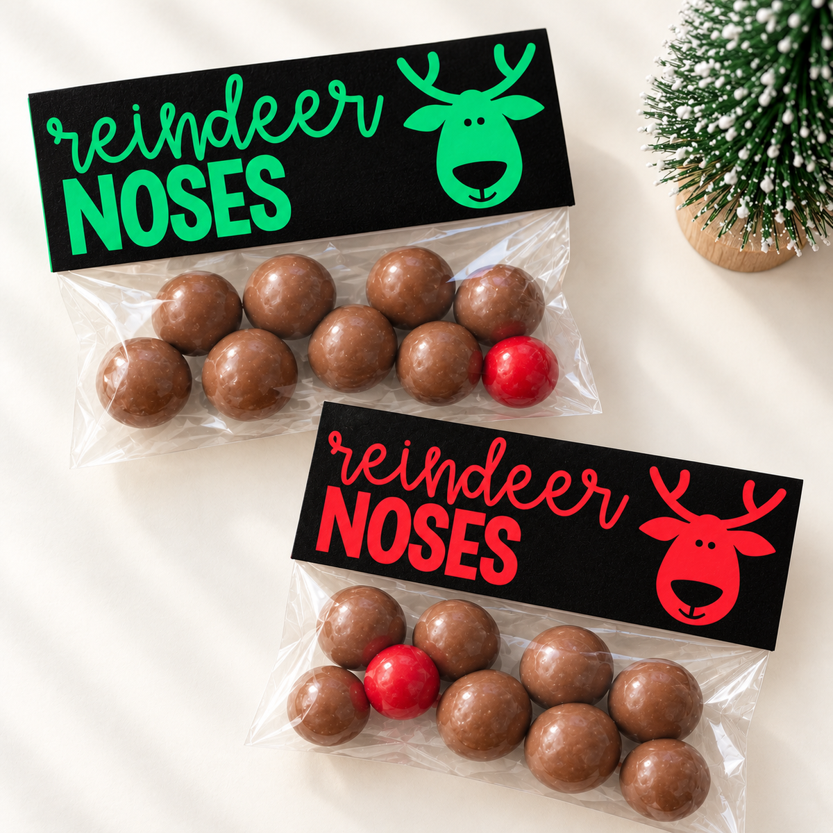 Two Reindeer Noses treat bags with printable bag toppers in red and green, filled with chocolate balls and a red nose