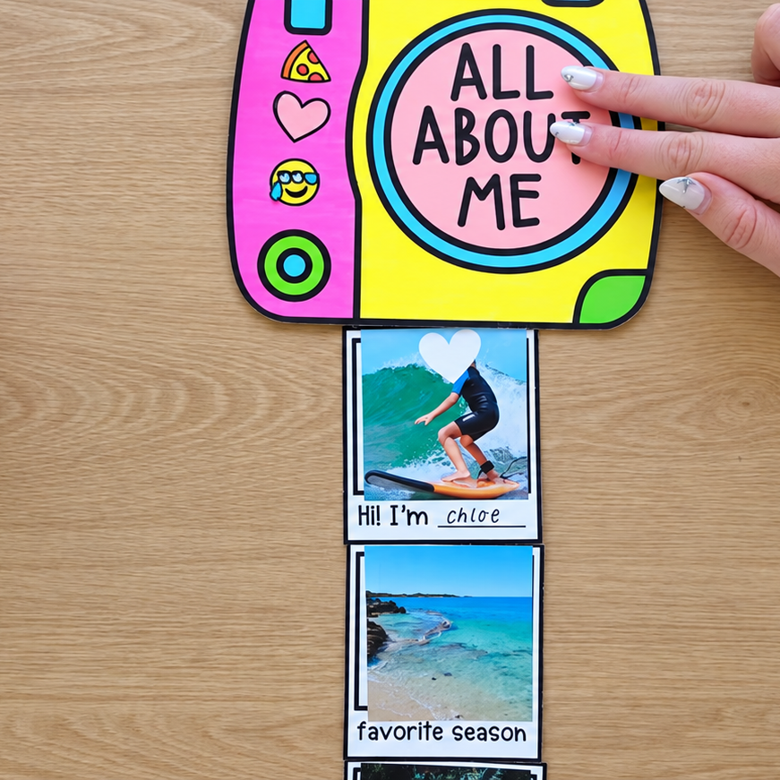 All About Me camera-shaped flip craft with photo cards, on a timber desk beside a pot of coloured pens