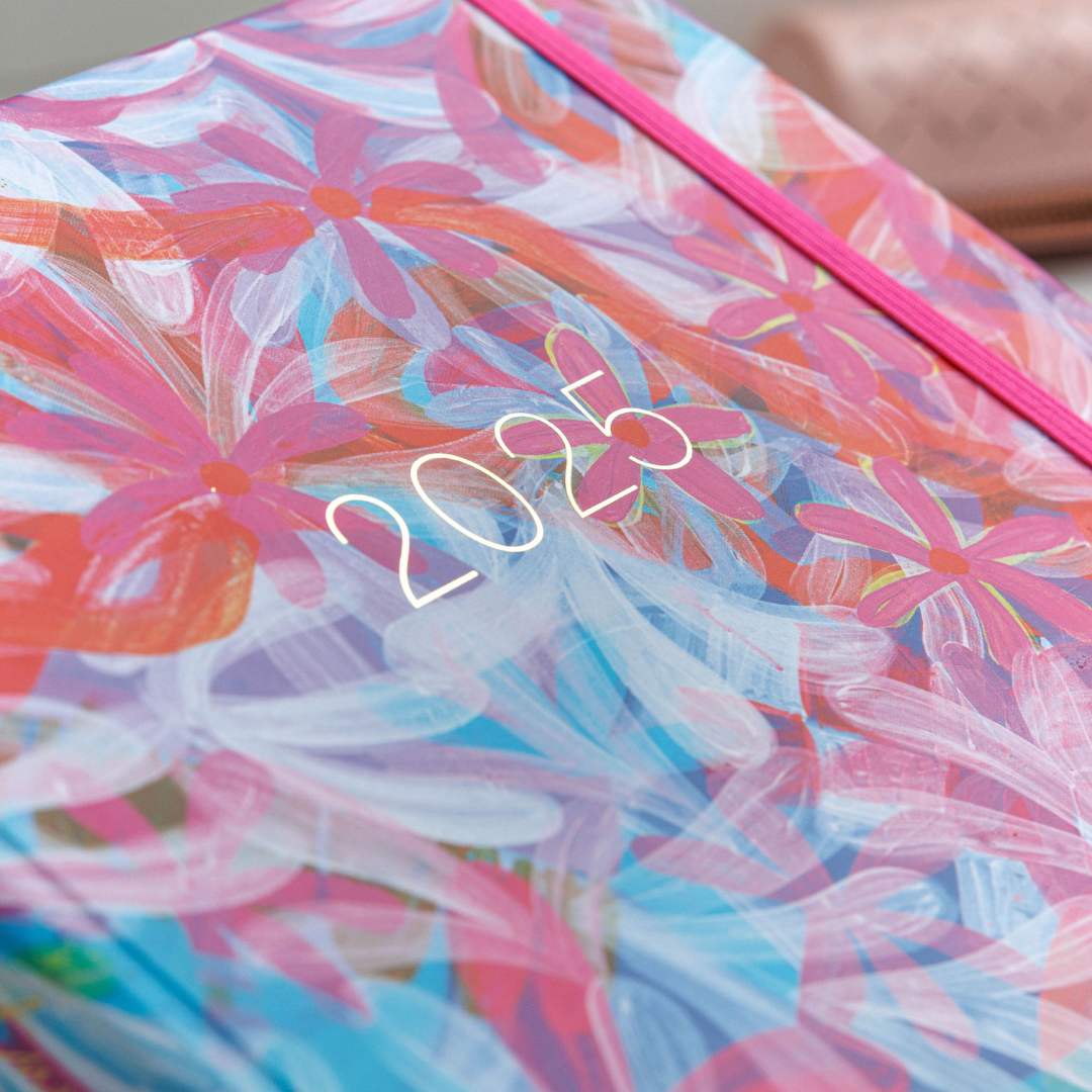 Close-up of the angled 'Upstream' personal planner, highlighting the gold '2025' text at the center and a pink elastic enclosure along the side.