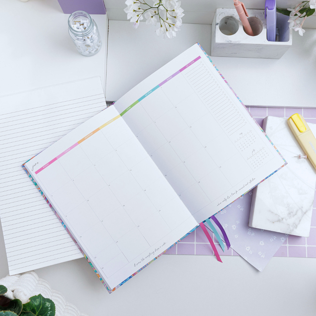Open 'Upstream' weekly planner lying on a desk, displaying the June calendar with weekdays highlighted in rainbow colours.