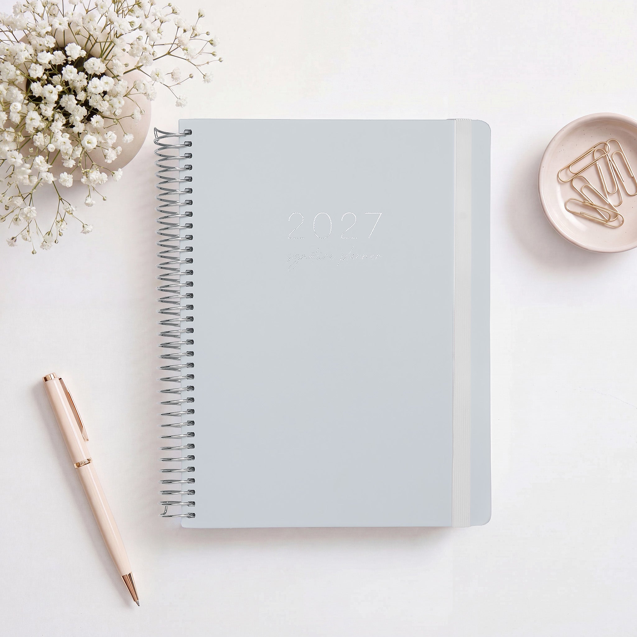 2027 Signature Planner in Dusk styled with baby's breath and a pink pen, silver coil and cream elastic closure.