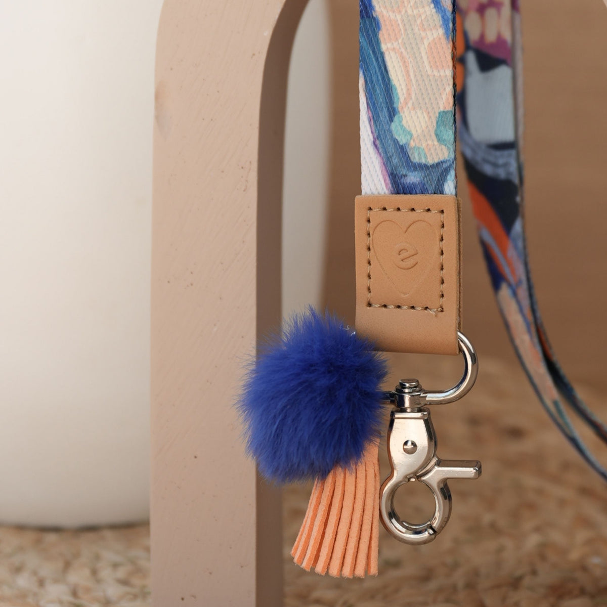Close up of Jewels teacher lanyard, abstract print, silver clasp, deep blue pom pom and orange tassel
