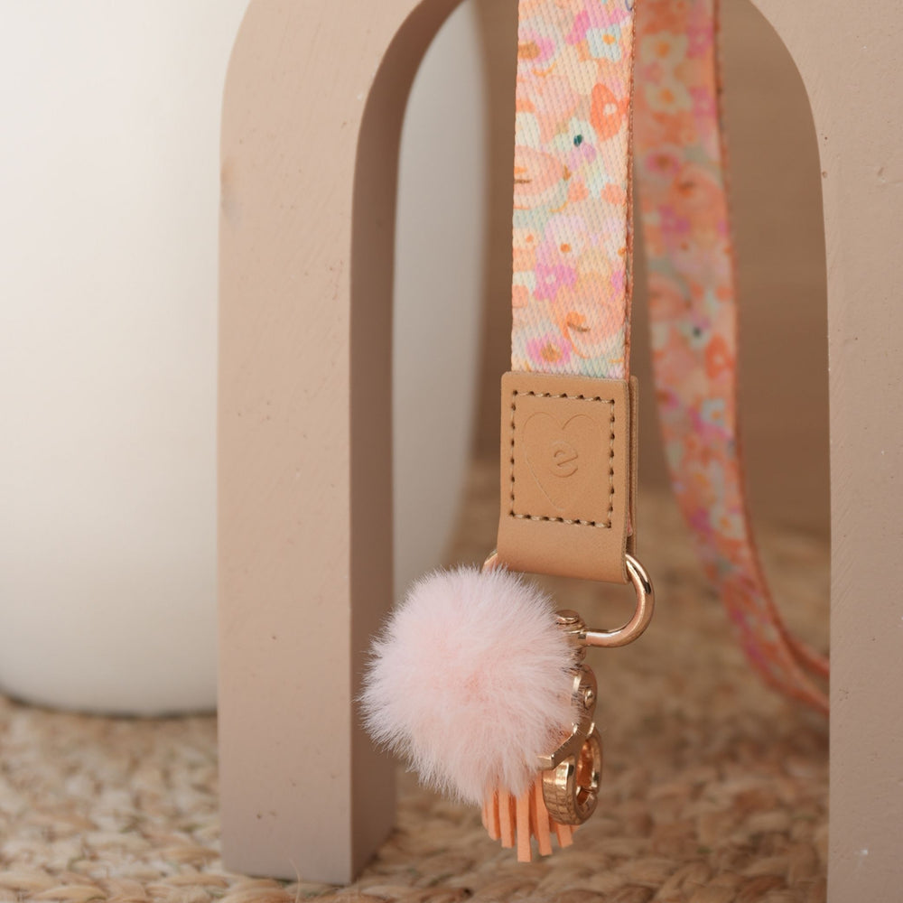 Close up of Love Fool teacher lanyard, pastel floral print, gold clasp, peach pom pom and orange tassel