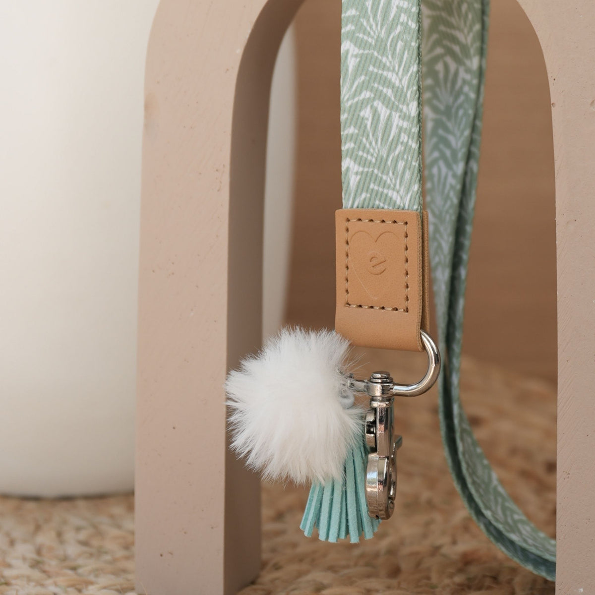 Close up of Olive Branches teacher lanyard, sage leaf print, silver clasp, white pom pom and mint tassel