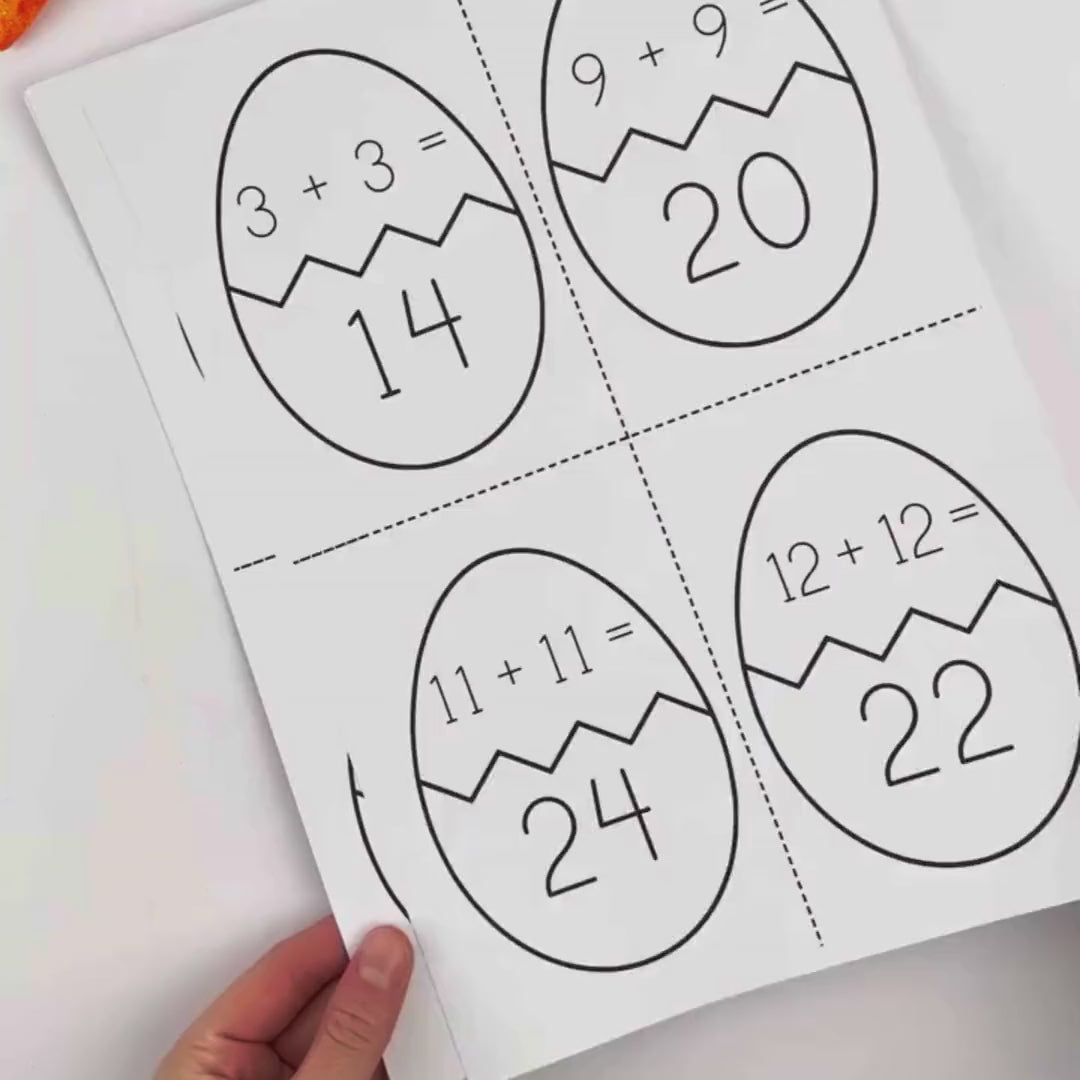 Four large eggs are divided with zigzag crack lines, each featuring an addition equation on the top half and a number on the bottom half. Examples include “3 + 3 = 14,” “9 + 9 = 20,” “11 + 11 = 24,” and “12 + 12 = 22.” Dotted cutting lines separate the eggs for a matching activity.
