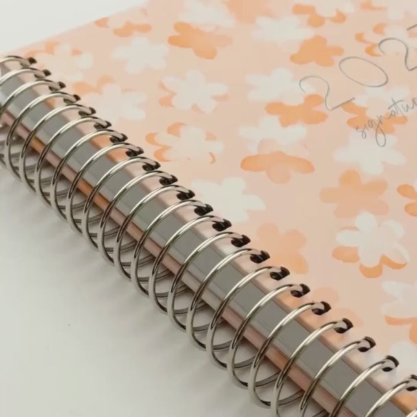 video of 2027 planner shades of orange and white florals design, peach elastic 