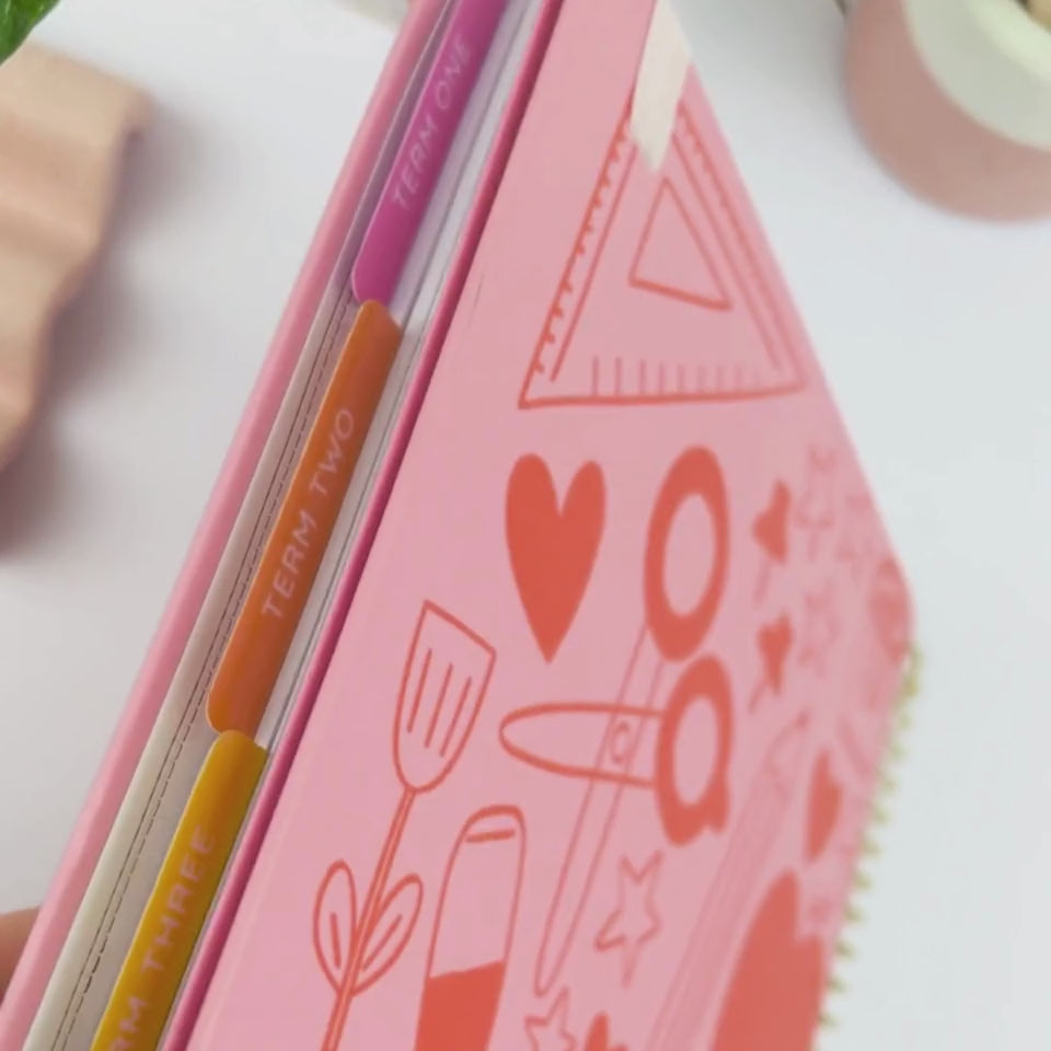 Front and back covers of the 2026 Hearts teacher planner being showcased on a white desk in a hands-on video demonstration.