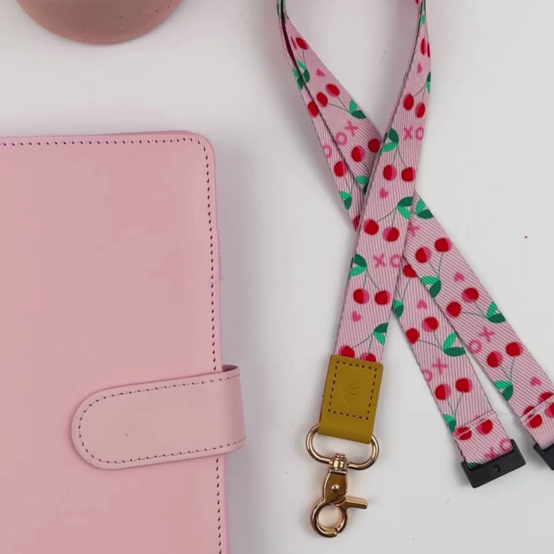 Hands displaying Pink cherries teacher lanyard with pink cherries design, gold clasp, and tan leather accent detail.