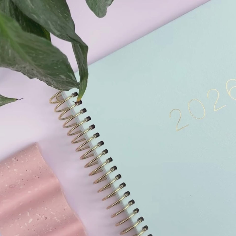 Front cover of the 2026 Mint teacher planner being showcased on a white desk in a hands-on video demonstration.