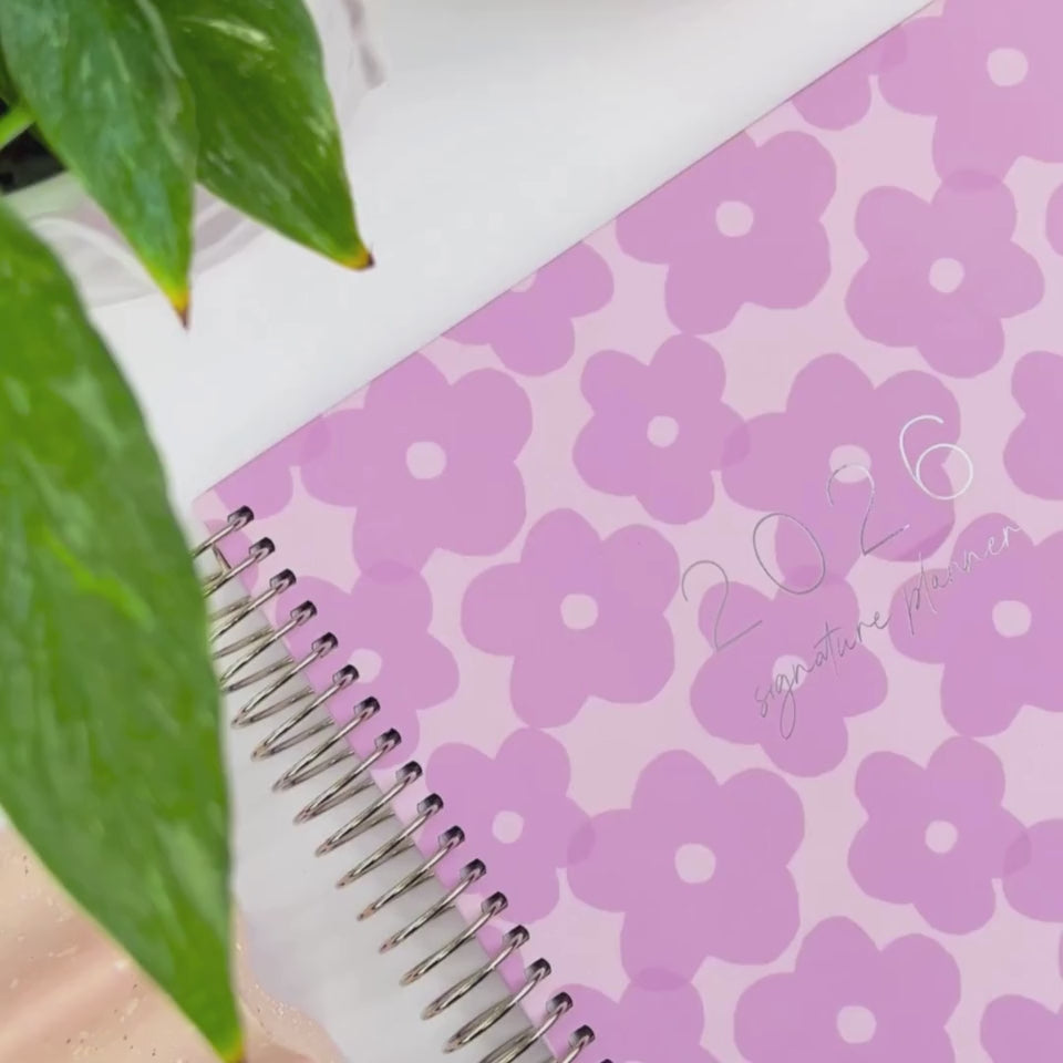 Front and back covers of the 2026 lilac flowers teacher planner being showcased on a white desk in a hands-on video demonstration.