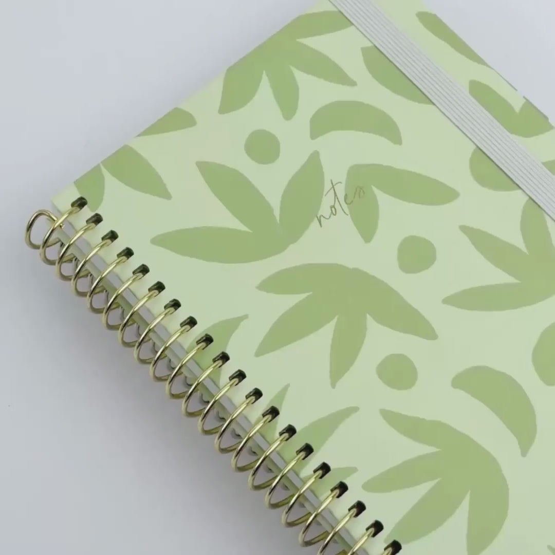 Sage green botanical spiral notebook with gold binding and elastic closure, shown from multiple angles in a product video.