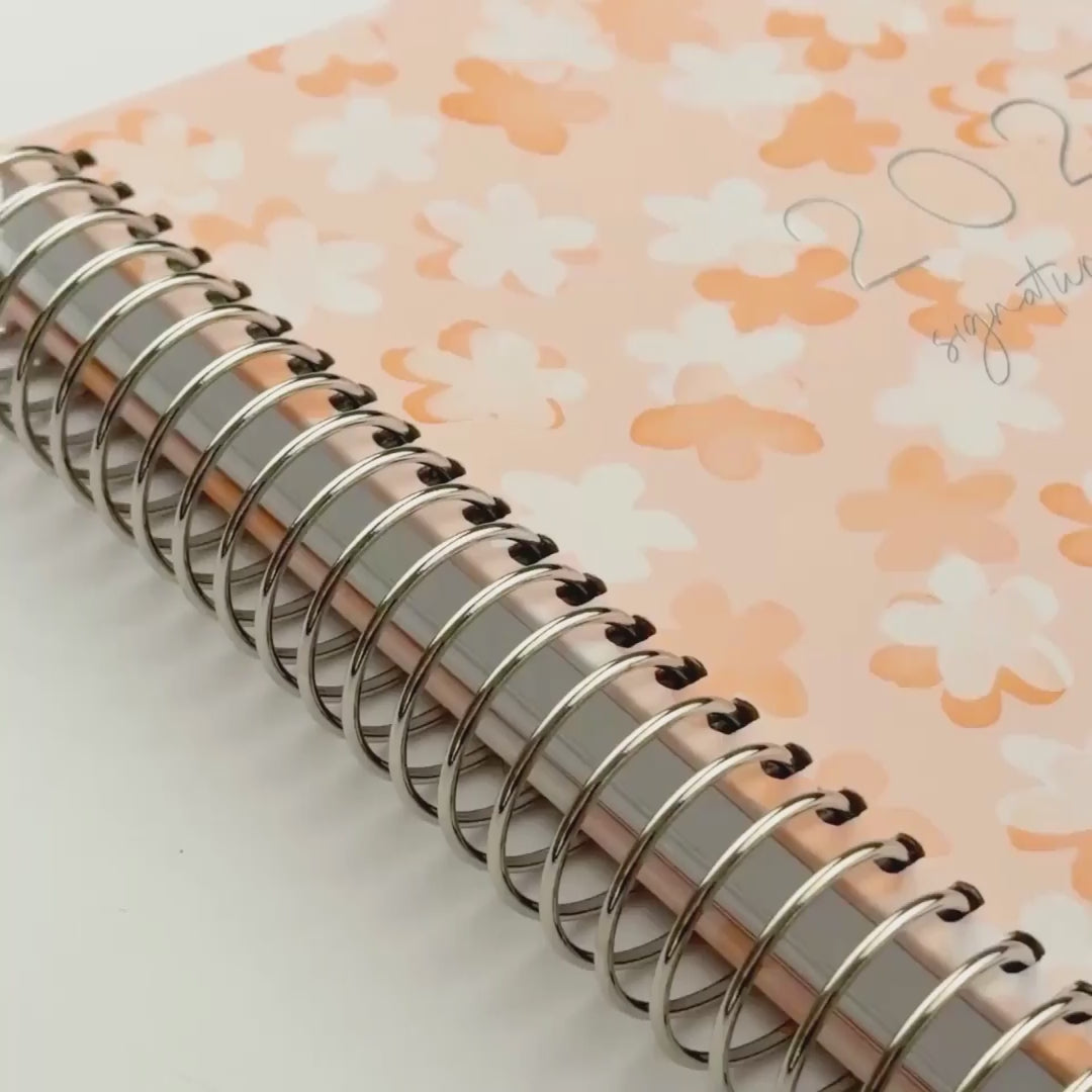 video of 2027 planner shades of orange and white florals design, peach elastic 