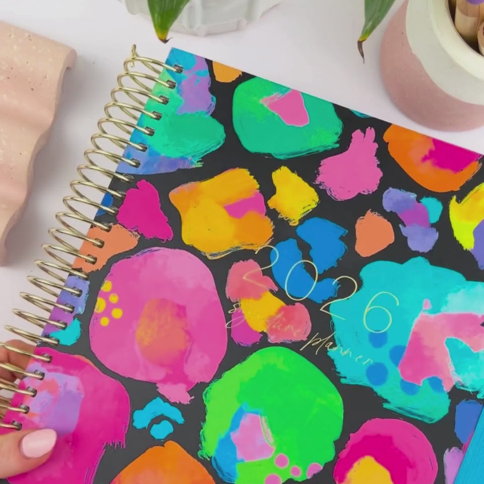 Front and back covers of the 2026 Rainbow Leopard teacher planner being showcased on a white desk in a hands-on video demonstration.