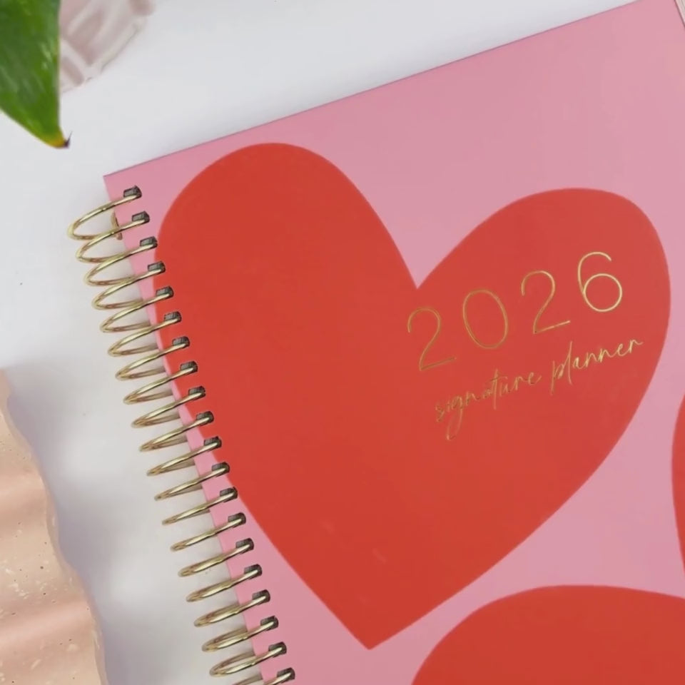 Front and back cover of the 2026 Hearts slimline teacher planner being showcased on a white desk in a hands-on video demonstration.