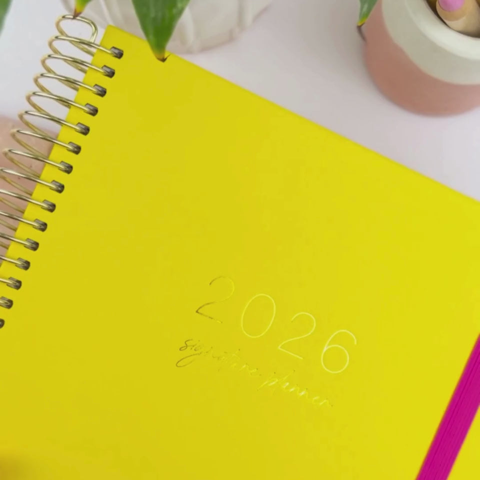 Hands flipping through the 2026 marigold teacher planner, showcasing cover design on a white desk.