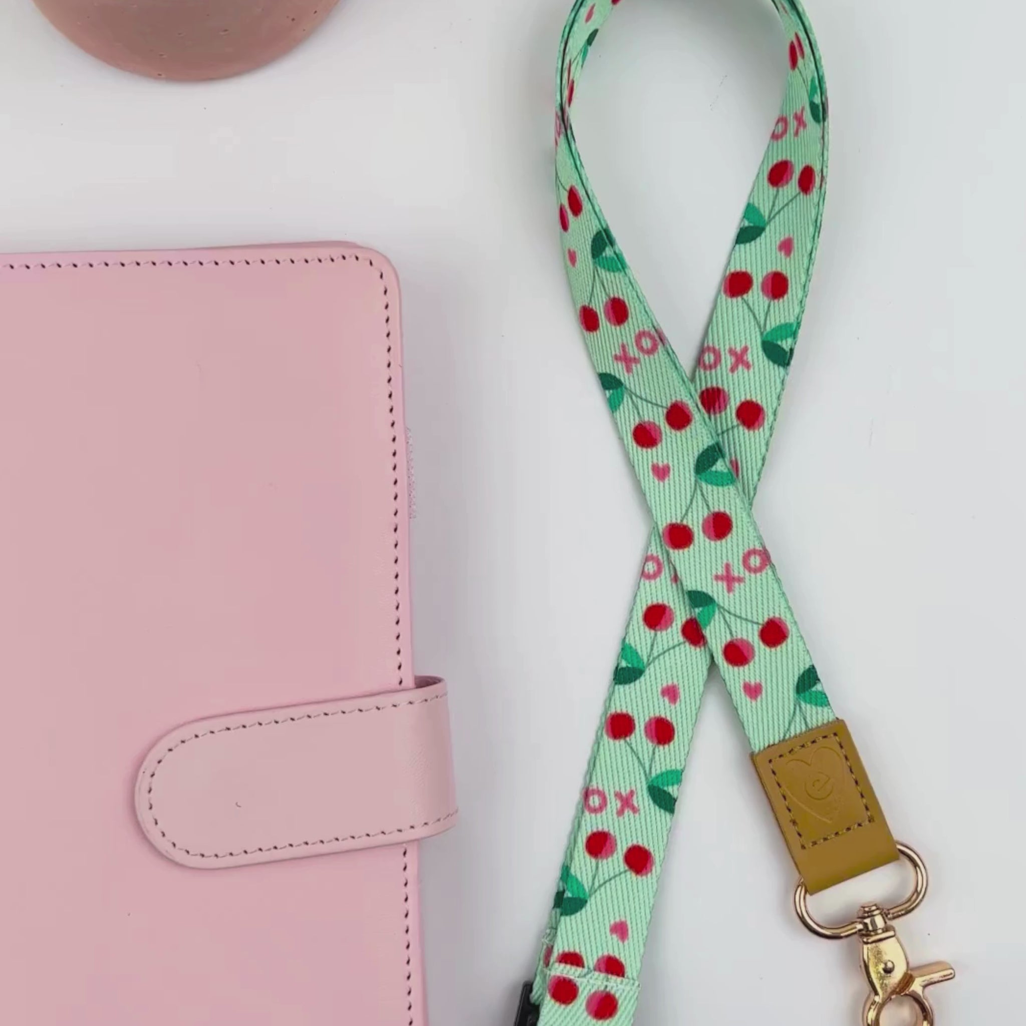 Hands displaying the Mint Cherries teacher lanyard with red cherries design, gold clasp, and tan leather accent detail.