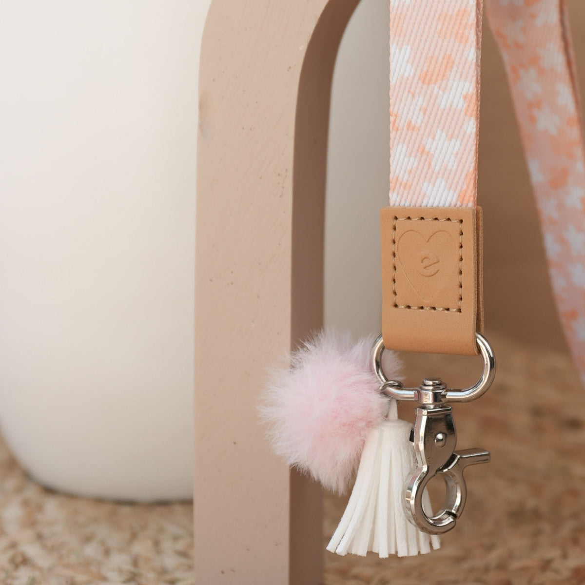 Close up of So Sweet teacher lanyard, peach floral print, silver clasp, peach pom pom and white tassel