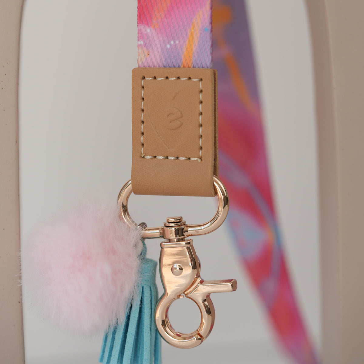 Detail of Solar Glow teacher lanyard clasp, gold hardware with baby pink pom pom and sky blue tassel
