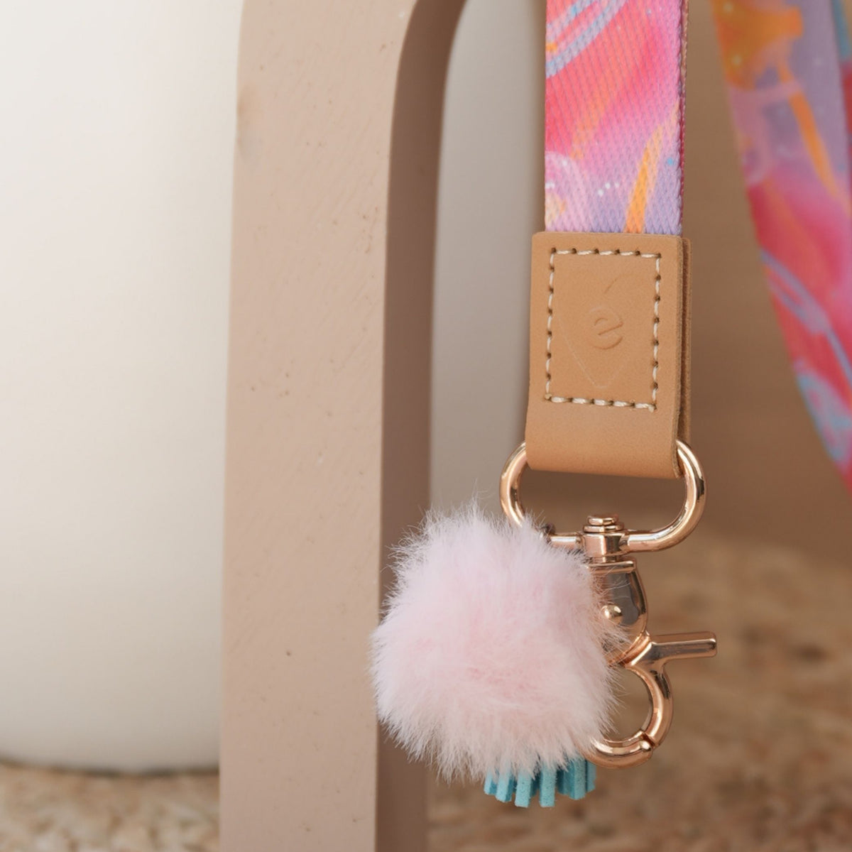 Close up of Solar Glow teacher lanyard, pink abstract print, gold clasp, baby pink pom pom, sky blue tassel
